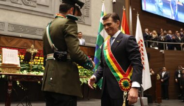 Der lächelnde Paz trägt die Schärpe, die er von einem Armeeangehörigen in Paradeuniform überreicht bekommen hat. Dahinter eine vollbesetzte Tribüne.