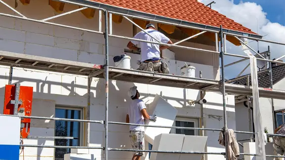 Bauarbeiter auf einem Gerüst bei der Dämmung einer Wohnhausfassade.