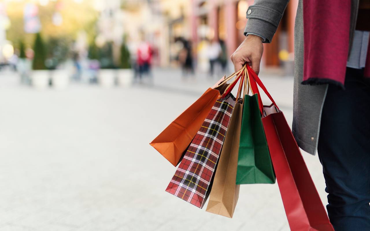 Verkaufsoffene Sonntage laden zum Shoppen ein. Ein unbekannter Mann hält vier unterschiedlich große Einkaufstüten in der Hand.