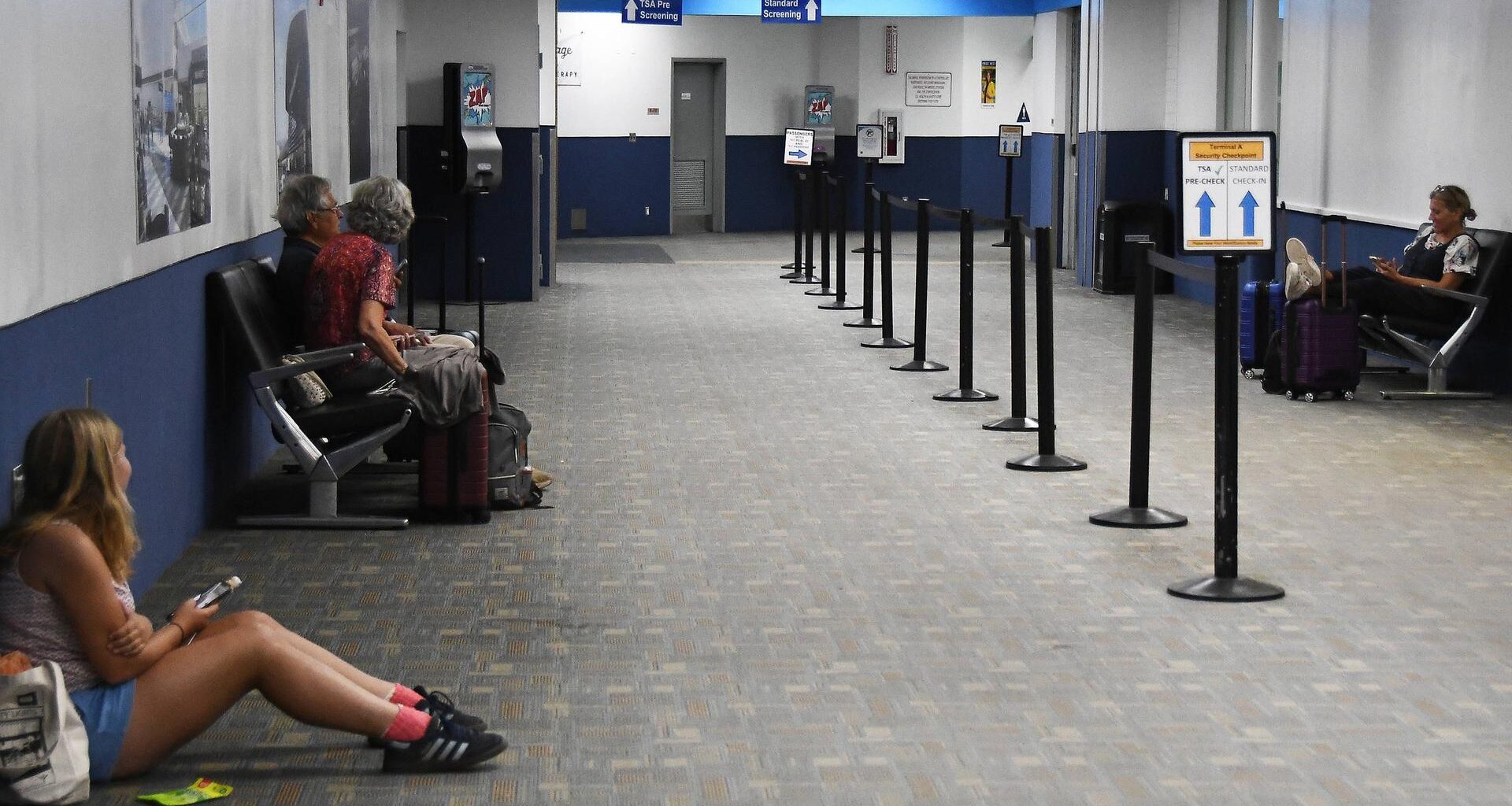 Menschen an einem Flughafen sitzen auf Bänken oder am Boden und warten.