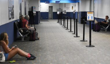 Menschen an einem Flughafen sitzen auf Bänken oder am Boden und warten.
