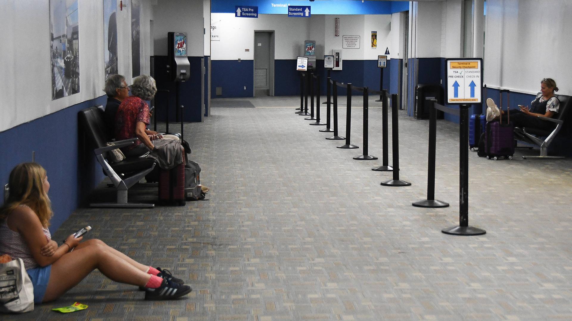Menschen an einem Flughafen sitzen auf Bänken oder am Boden und warten. Menschen an einem Flughafen sitzen auf Bänken oder am Boden und warten.