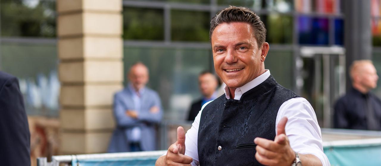 Stefan Mross posiert selbstbewusst lachend auf einem roten Teppich in die Kamera.