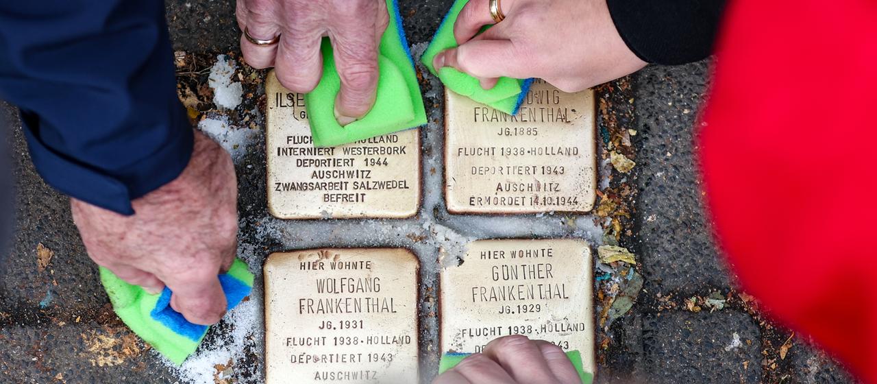 Menschen putzen vier Stolpersteine.