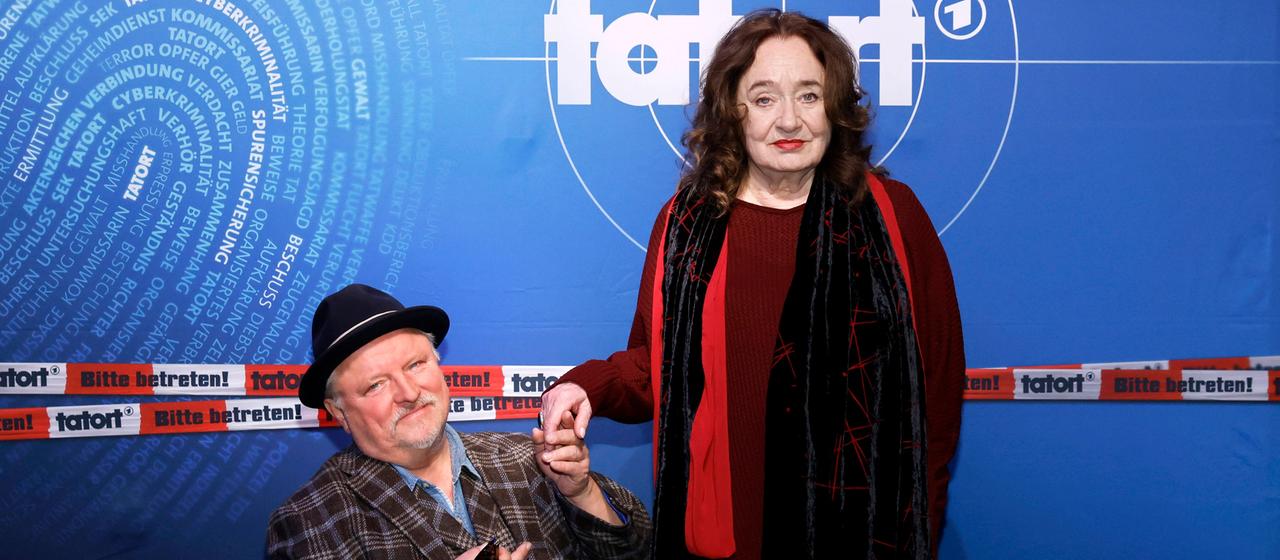Schauspieler Axel Prahl und Schauspielerin Mechthild Großmann, im Hintergrund Tatort-Logo | IMAGO / Panama Pictures Schauspieler Axel Prahl und Schauspielerin Mechthild Großmann, im Hintergrund Tatort-Logo