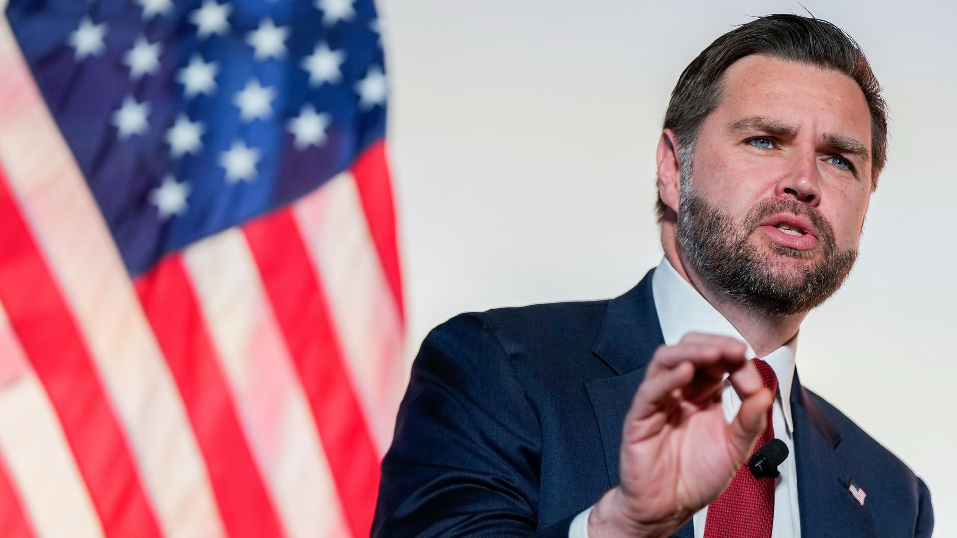 Der bärtige Vance spricht vor einer amerikanischen Flagge. Im Hintergrund eine weiße Wand. Er trägt ein schwarzes Jackett. Der bärtige Vance spricht vor einer amerikanischen Flagge. Im Hintergrund eine weiße Wand. Er trägt ein schwarzes Jackett.