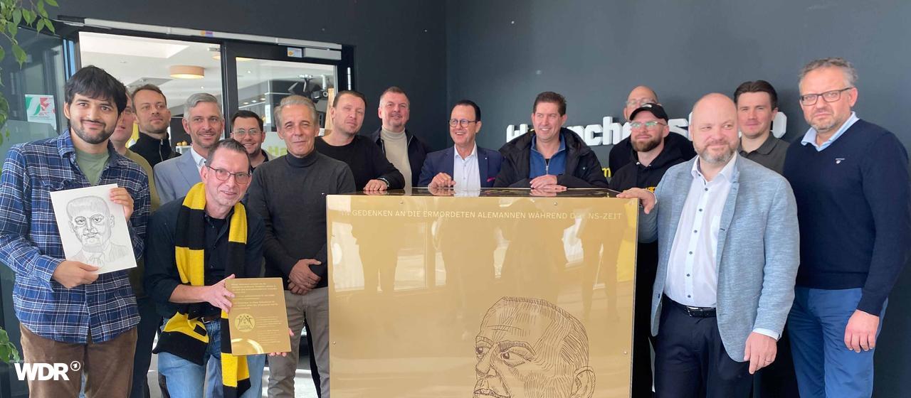 Mehrere Personen stehen hinter dem Gedenkstein. Auf diesem steht "IN GEDENKEN AN DIE ERMORDETEN ALEMANNEN WÄHREND DER NS-ZEIT"