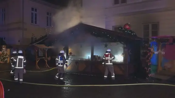 Feuerwehrleute löschen eine brennende Hütte auf einem Weihnachtsmarkt 