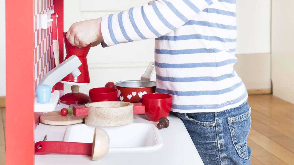 Junge (4) klemmt mit Kopf in Spielküche