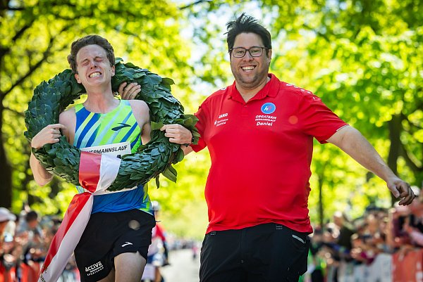 Schon beim Zieleinlauf fließen bei Florian Bochert die Tränen. Orgateam-Leiter Daniel Skakavac freut sich, seinem Vereinskollegen den Kranz überwerfen zu dürfen. - © Sarah Jonek