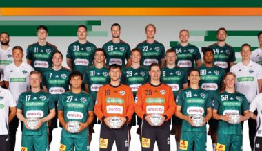 Eine Handballmannschaft der Männer posiert für ein Gruppenfoto in grünen Trikots mit Mitarbeitern in weißen Hemden, die Handbälle halten, vor einem Hintergrund mit grünen und orangefarbenen Streifen.