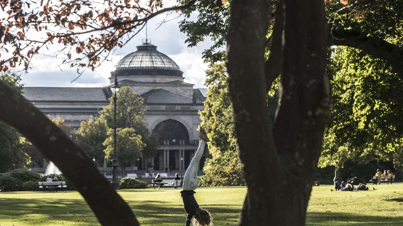 Der Kurpark in Wiesbaden. Im Hintergrund die Hinteransicht des Kurhauses. ein Mädchen schlägt ein Rad im Gras. Der erste Bauabschnitt betrifft etwa 200 Meter des Rambachkanals – vom Kurpark bis zur Wilhelmstraße.
