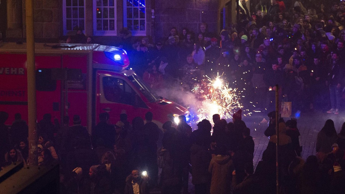 Ein Rettungswagen fährt kurz nach Mitternacht mit Blaulicht auf der Straße vor den Hamburger Landungsbrücken während neben ihm Pyrotechnik explodiert. Silvester-Feuerwerk in Hamburg