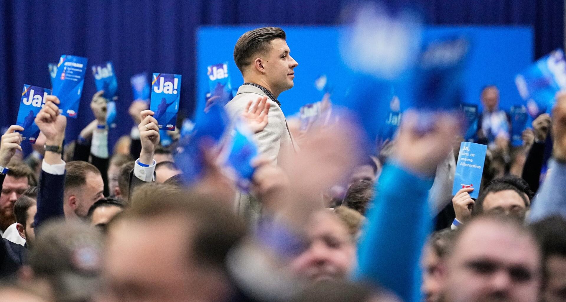 Jean-Pascal Hohm, Vorsitzender der "Generation Deutschland", im Vordergrund blaue AfD-Stimmkarten und Gesichter.