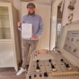 Bester Laune: Kevin Nikodem präsentiert die Baugenehmigung für den Umbau des Wirxel-Hauses. Der Vorsitzende des 50er-Jahre-Museums steht in dem ehemaligen Behandlungszimmer der Wirxel-Praxis, rechts steht ein EKG aus dem Jahr 1954.