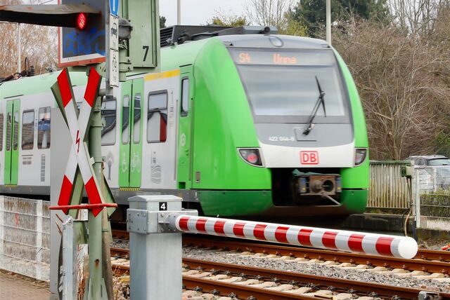 Ein grüner Zug fährt auf den Schienen in eine Station, während ein André-Logo sichtbar ist.
