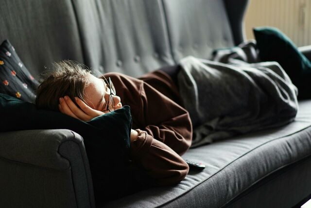 Eine Person liegt auf einem Sofa. Sie hat eine Decke über den Beinen.