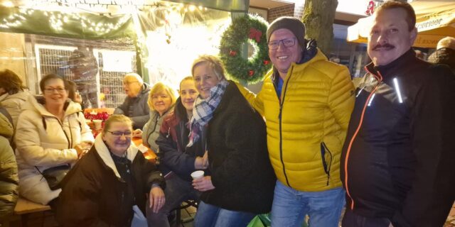 Gruppenfoto von Menschen, im Hintergrund Weihnachtsbeleuchtung und ein Kranz.