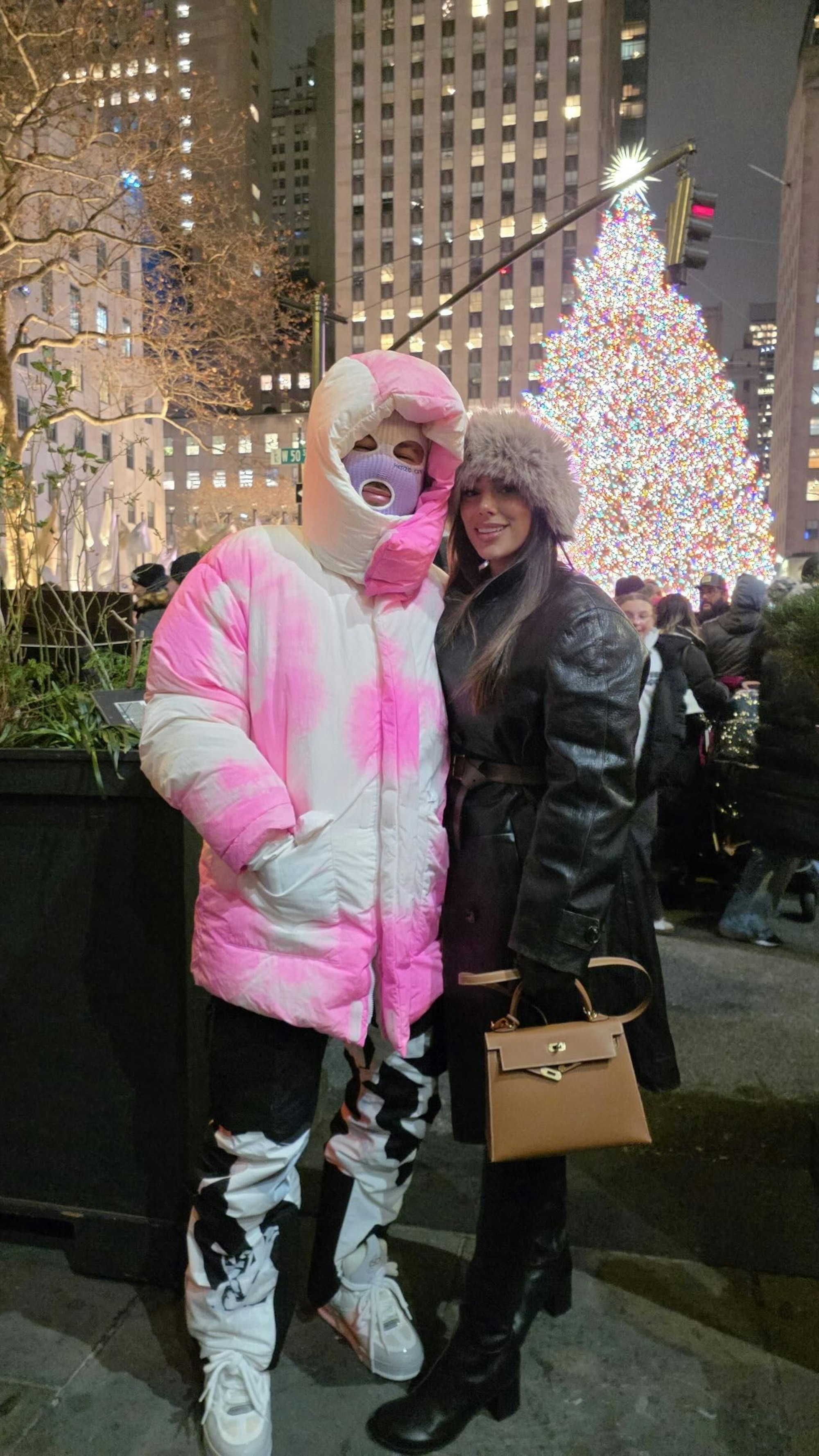 Neymar in weiß-pinker Winterjacke und Skimaske gemeinsam mit seiner Freundin vor einem Weihnachtsbaum in New York.
