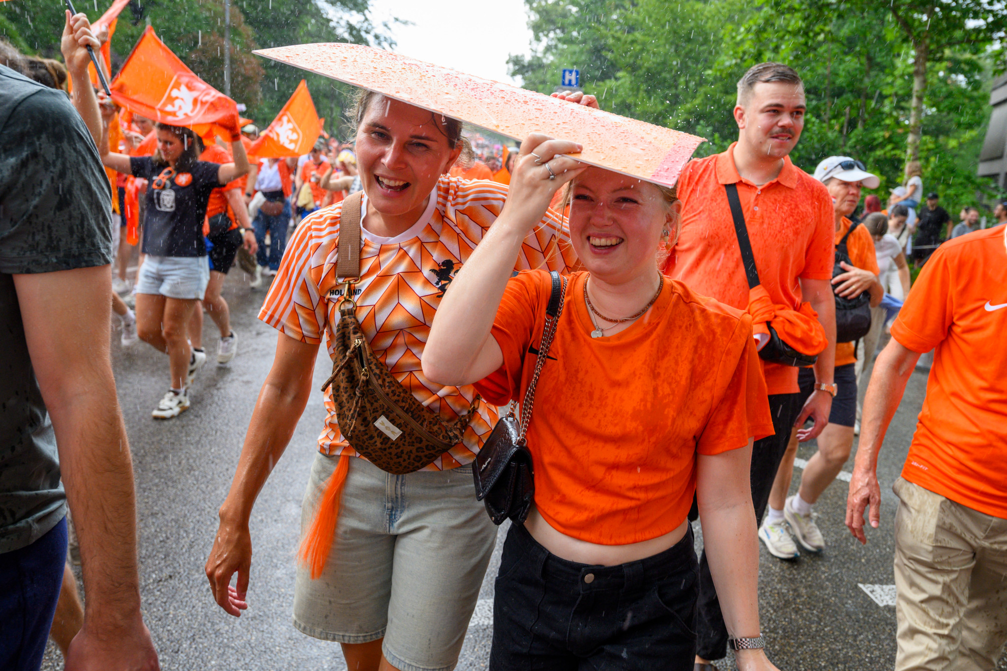Fans in orange Kleidung bei einem Fanmarsch am Barfüsserplatz in Basel während der EURO Holland Frankreich am 13. Juli 2025. Sie schützen sich mit einem Schild vor Regen.