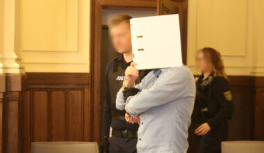 Angeklagter mit Sichtschutz betritt mit Wachtmeistern Gerichtssaal.