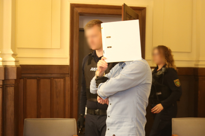 Angeklagter mit Sichtschutz betritt mit Wachtmeistern Gerichtssaal.