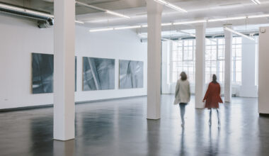 Zwei Menschen in einer Halle. An der Wand hängen Bilder.