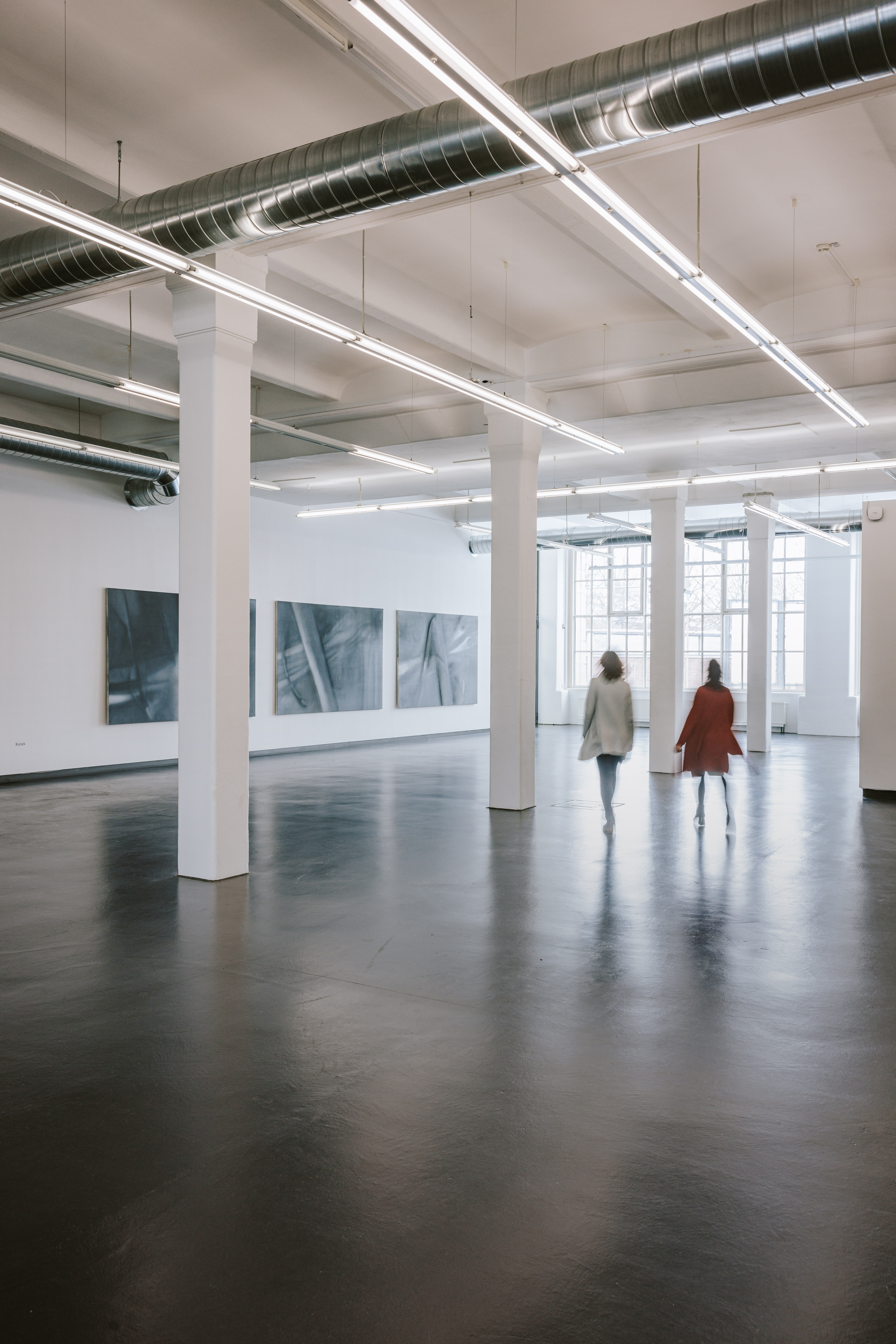 Zwei Menschen in einer Halle. An der Wand hängen Bilder.