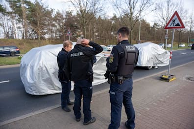 Polizisten stehen vor den abgedeckten Wagen. Unter den Planen verbergen sich vermutlich Prototypen von Audi.