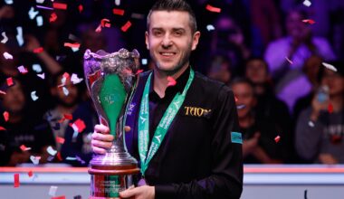 Mark Selby hält lächelnd die Trophäe der UK Championship, während Konfetti auf ihn herunterregnet.