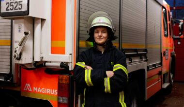Feuerwehrfrau Nora Tenbusch steht vor einem Einsatzwagen der Feuerwehr. Sie trägt die Schutzkleidung der Feuerwehr und hat einen Helm auf dem kopf. Sie schaut in die Kamera und hat ihre Arme verschränkt.
