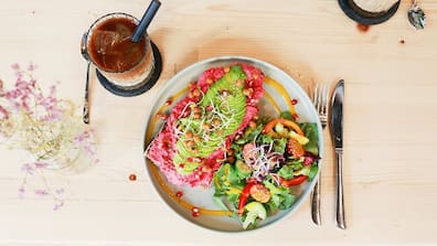 Iced Latte und Frühstücksteller „Just Beet It“ mit roter Beete Hummus, Avocado, gerösteten Kichererbsen, Sesam und Sprossen auf Sauerteigbrot, dazu ein frischer Salat.