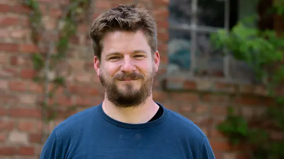 NDR Kultur Literaturredakteur Alexander Solloch vor einer Backsteinwand.