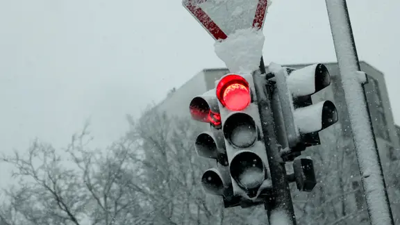 Eine rote Ampel und ein Verkehrsschild sind stark verschneit.