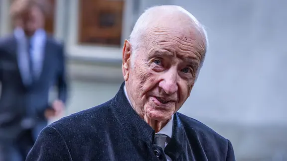 Armin Mueller-Stahl steht im Mantel auf der Straße und blickt in die Kamera.