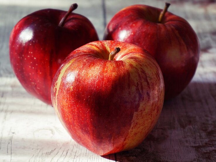 Drei rote Äpfel auf einem Brett. | © Pexels/ Suzy Hazelwood via Canva.com