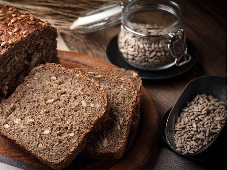 Auf einem Brett liegt ein Brot und eine Scheibe Vollkorntoast. | © Getty Images Pro/ arfo via Canva.com