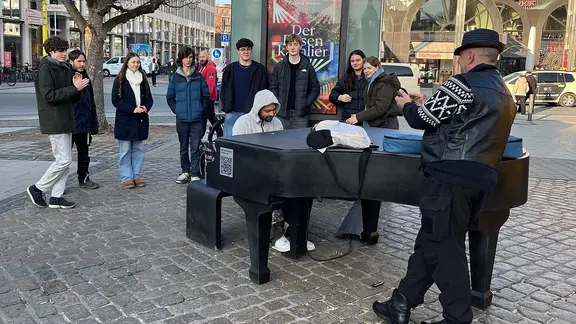 Menschen umringen ein Klavier auf einem Platz