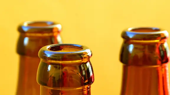 Drei leere Bierflaschen stehen vor einem gelben Hintergrund.