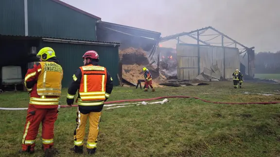 Feuerwehrleute stehen vor der abgebrannten Halle in der Nähe von Gadebusch. 