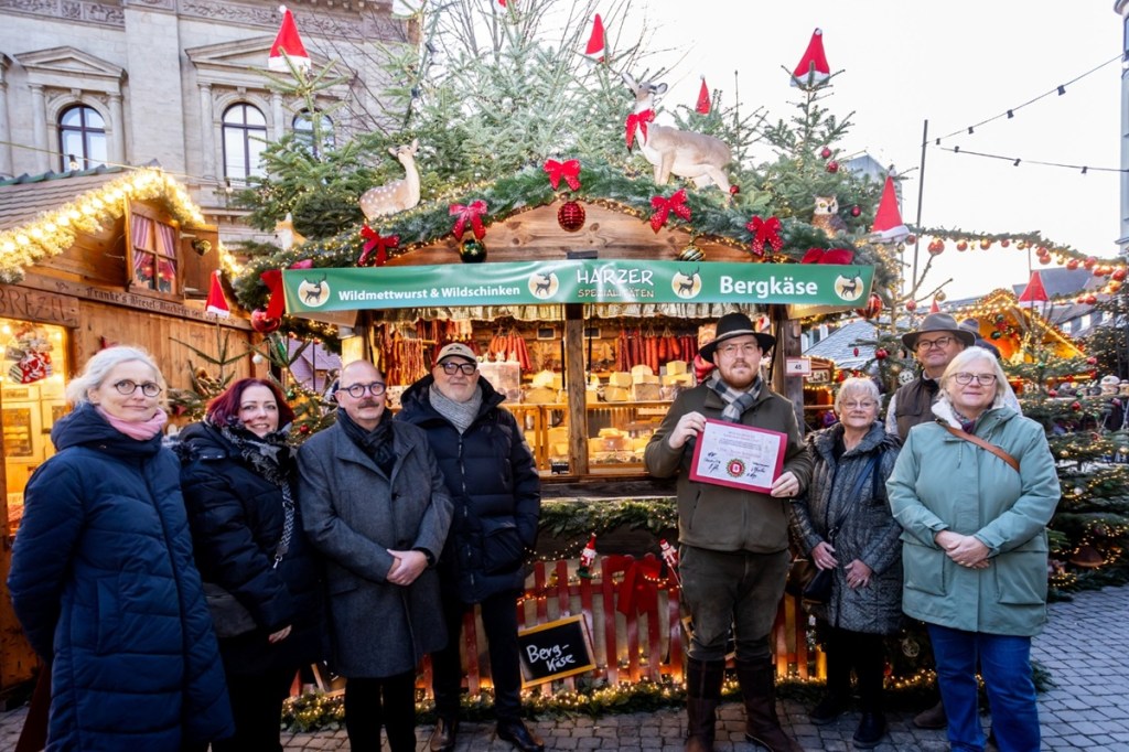 Der schönste Stand auf dem Braunschweiger Weihnachtsmarkt 2025 steht fest: „Harzer Spezialitäten“ bekommt in diesem Jahr die Auszeichnung überreicht: (v. l. n. r.) Cornelia Götz, Carolin Illmer, Karsten Ziaja, Olaf Jaeschke, Standbetreiber Franko Almstadt, Ulrike Neumann, Thomas Bronswyk und Bezirksbürgermeisterin Jutta Plinke.