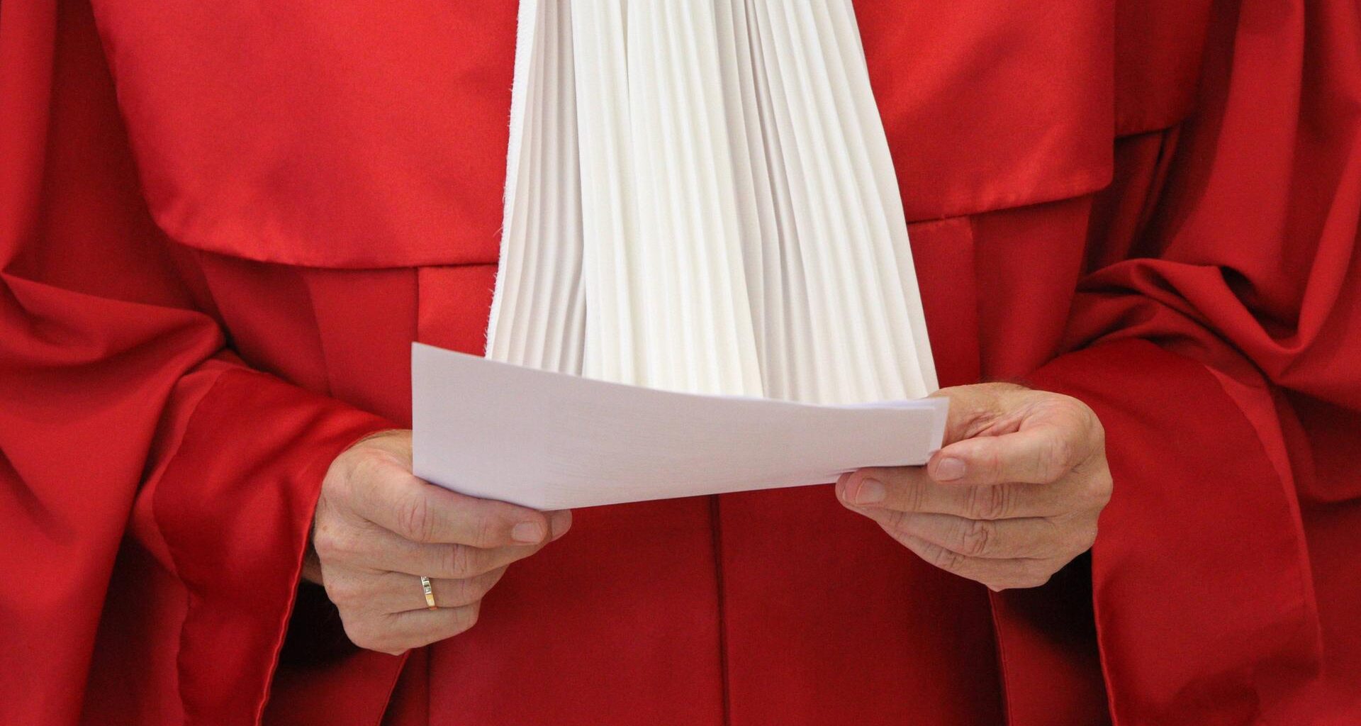 Die rote Robe eines Richters des Bundesverfassungsgerichts. Die Person hält ein Papier in der Hand. Kopf und Beine sind nicht zu sehen.