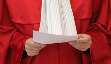 Die rote Robe eines Richters des Bundesverfassungsgerichts. Die Person hält ein Papier in der Hand. Kopf und Beine sind nicht zu sehen.