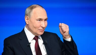 Russlands Präsident Putin steht vor einem blauen Hintergrund und hebt die linke Hand zur Faust.