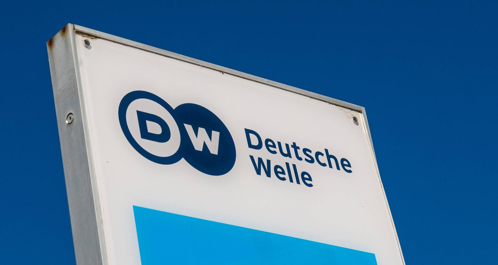 Das Logo der Deutschen Welle auf einem Schild, dahinter blauer Himmel.
