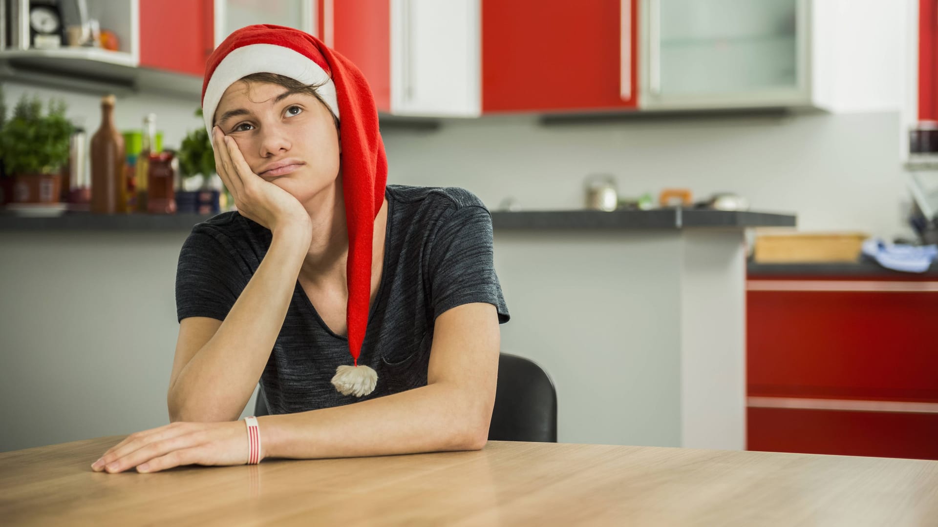 Ein Mann mit Weihnachtsmütze sitzt alleine in einer Küche (Symbolbild):