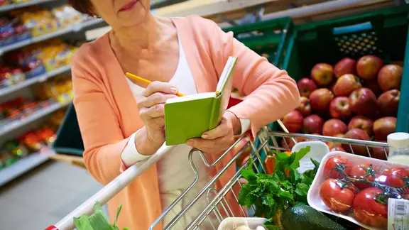 Eine Frau mit vollem Einkaufswagen und Notizbuch in der Hand.