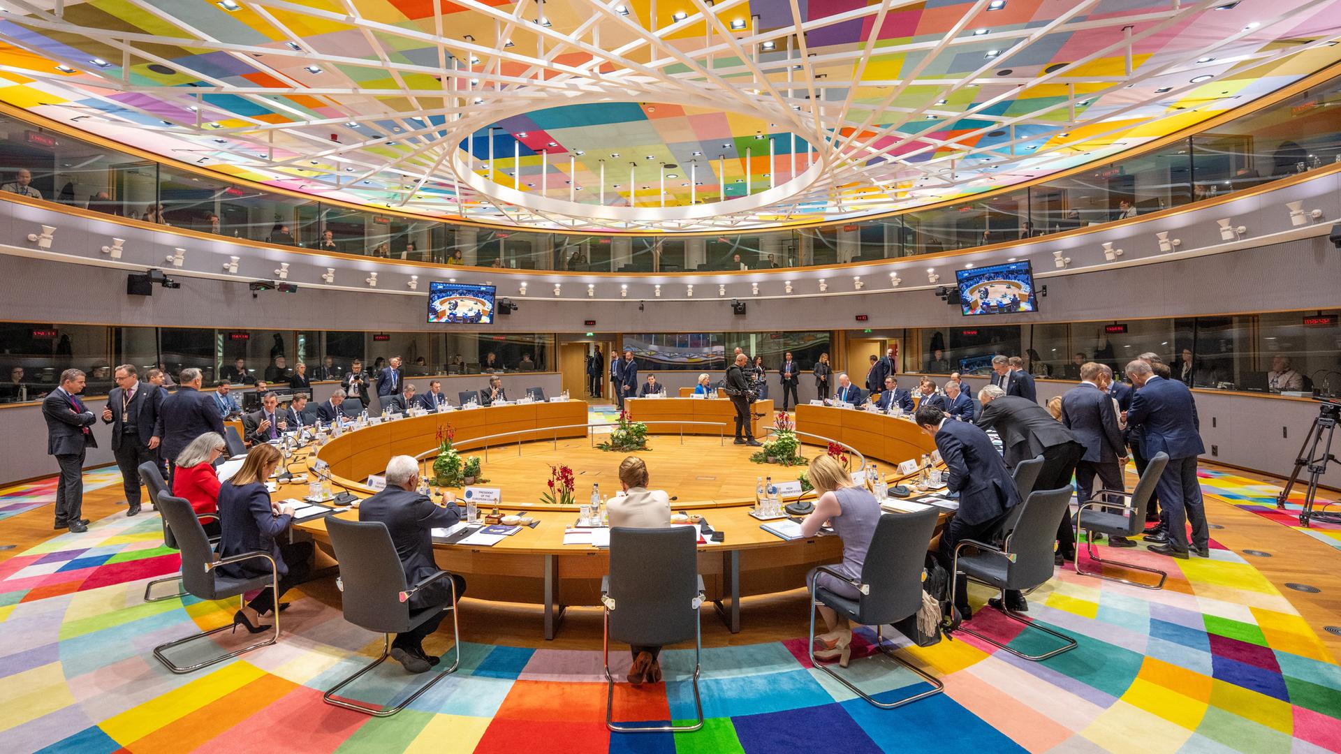 Eine große Gruppe Politikerinnen und Politiker versammelt sich in einem Sitzungssaal an einem großen, runden Tisch.