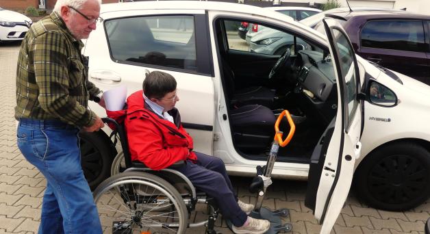 Der 76-jährige Ehemann hilft der Ehefrau auf das Drehgestell (roter Griff) und damit auf den Beifahrersitz. Dazu muss die Tür ganz geöffnet sein.