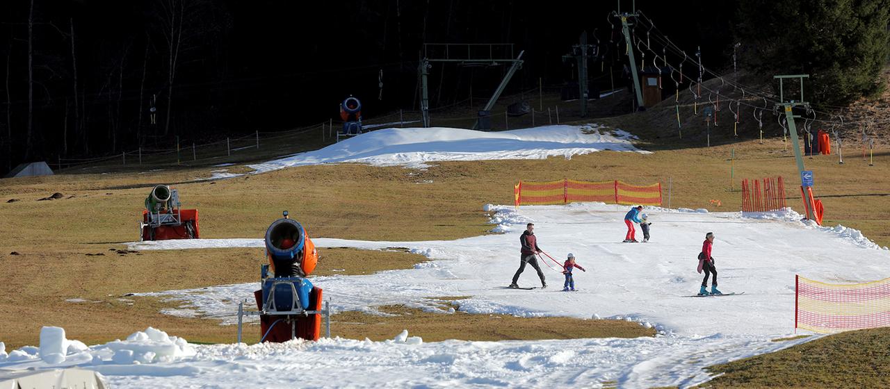 Skifahrer üben an einer Skipiste auf dem von Schneekanonen produzierten Kunstschnee.